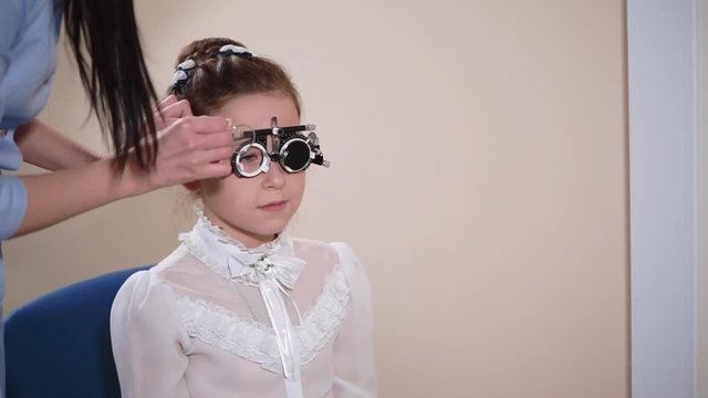 Portrait of a young girl wearing eye test glasses on her head at ophthalmologist. Doctor changing lenses to find the right ones.