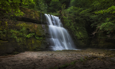 Obraz premium The Sgwd Clun Gwyn waterfall, a huge ledged waterfall on the Mellte river, near the village of Pontneddfechan in South Wales, UK. 