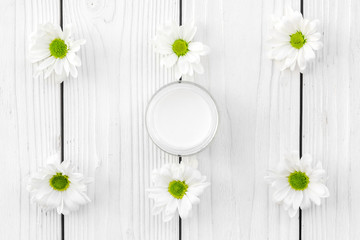 Obraz premium Chamomile cream. Face and body care. Cosmetics in small jar near chamomile flowers on white wooden background top view pattern