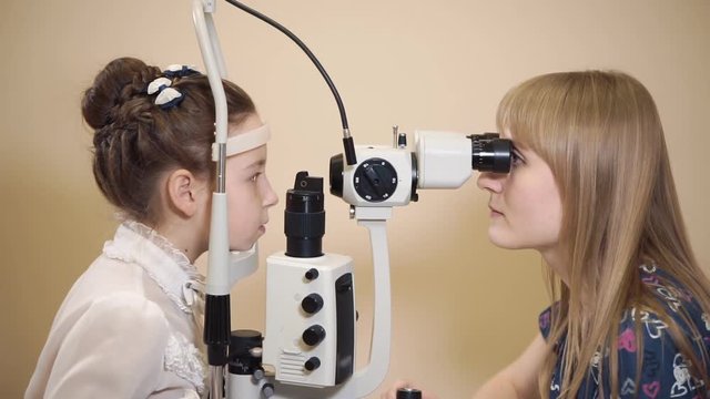 Female oculist checking eyes of young girl at the office. Ophthalmologist using slit lamp for examination.