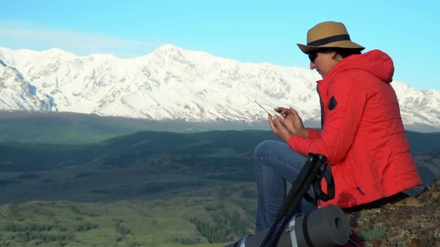 The woman the traveler sits on the rock and photographs snow mountains on the smartphone.