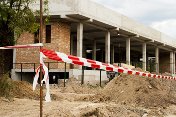 Red and white barrier tape near construction site against the sky. Concrete building development....