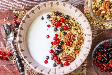 Bowl of homemade granola with yogurt and fresh berries on wooden background from top view