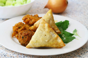 Plate full of Indian samosas, pakoras and onion rings with fresh coriander leaves on the side
