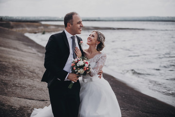 Happy bride and groom walk by the beach - Powered by Adobe