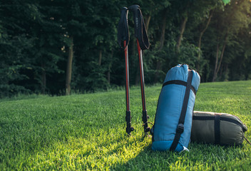 tourist lifestyle , two sleeping bags trekking poles on green grass illuminated by sunlight