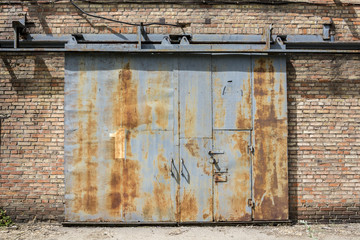 Sliding the rusty iron gate with the number one written with white paint a brick wall.