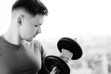 Close up of young pretty athletic man training biceps with dumbbell. Healthy lifestyle concept.