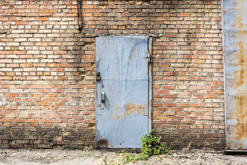 A rusty iron door with peeling blue paint on a brick wall.
