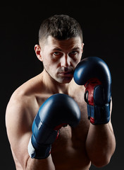 Low key studio portrait of handsome muscular fighter practicing boxing on dark blurred background