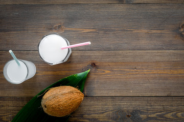 Tropical alcohol-free beverage. Fresh coconut milk in glasses with straw near coconut and palm leaves on dark wooden background top view copy space