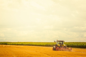 Naklejka premium Agriculture - green tractor ploughing at the field on a sunny day