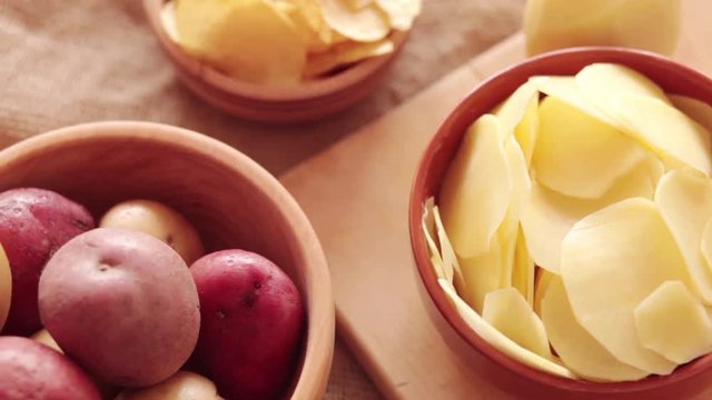 Raw potato in wooden bowl with chips and thin slices at rotating stand. Close-up, no people