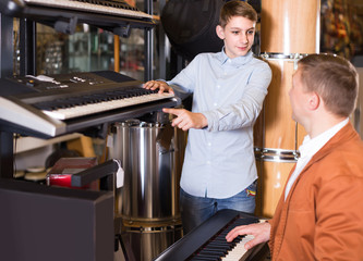 Father and teenage son examining keyboards in guitar shop