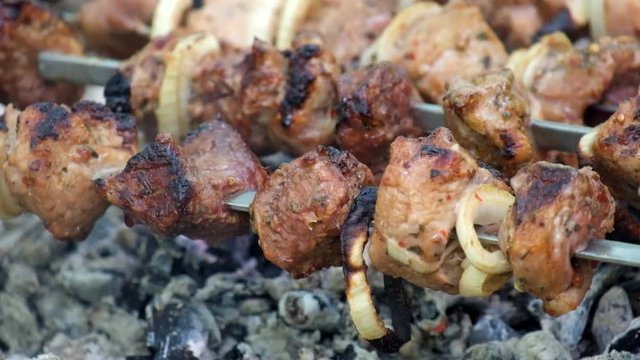 Shish kebab on skewers in the forest. Juicy pieces of meat are roasted on coals