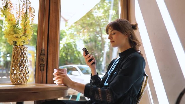 Happy girl relaxing in a cafe sitting at window, use smartphone