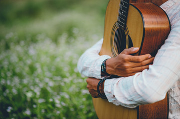The man's hand plays the acoustic guitar, plays the guitar in the garden alone, happily and loves the music.