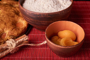 A bowl with flour and apricot cake on a wooden background