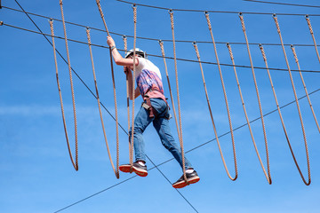 Teenager climbing on track with obstacles in adventure park.