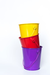 Purple, red, and yellow metal pails stacked together solid white background