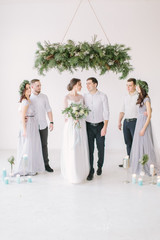 Happy newlyweds with bridesmaids and groomsman posing in white decorated studio