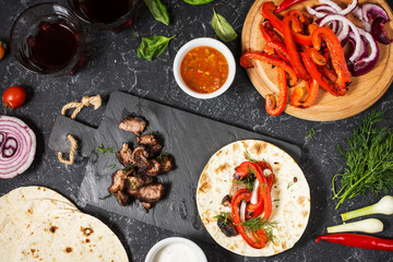 Fresh delicious mexican tacos and food ingredients on black stone background. Cooking.
