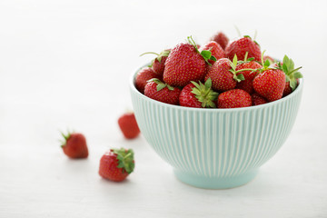 Light blue bowl with fresh juicy strawberry on white table.