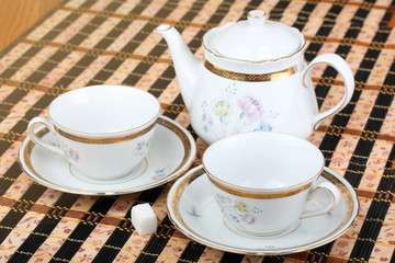 Two empty white porcelain cup and teapot on the table covered with striped bamboo table mat