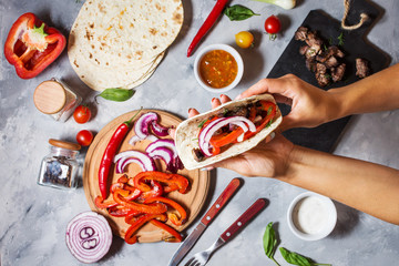 Female hands hold mexican tacos on concrete background. Cooking.