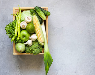 Green vegetables fruit in wooden box on grey background.