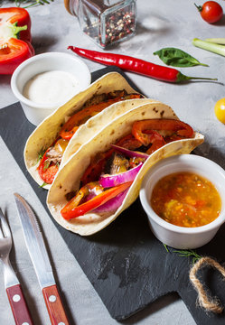 Fresh delicious mexican tacos and food ingredients on concrete background