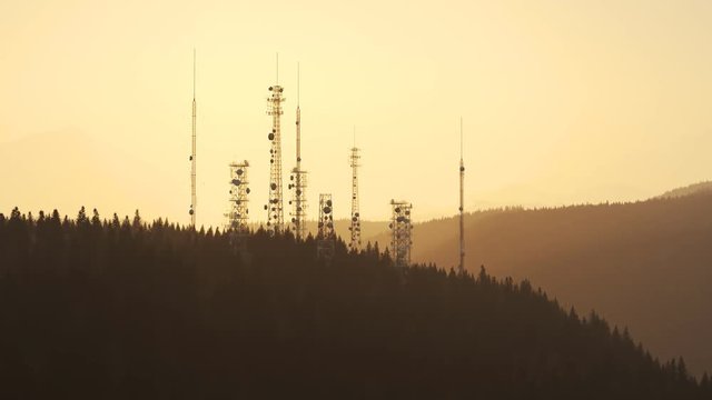 Antennas complex on a forested hill. Radio masts for telecommunication. Sunset.