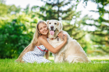 Little girl sitting on the grass with golden retriever dog in the summer park