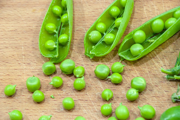 Fresh pods of sweet green peas in basket, on wooden board.
