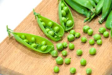 Fresh pods of sweet green peas in basket, on wooden board.