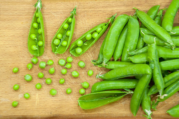 Fresh pods of sweet green peas in basket, on wooden board.