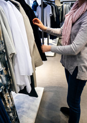 Woman shopping for beautiful modern clothes in upscale casual fashion store - selecting for the trench overcoat 