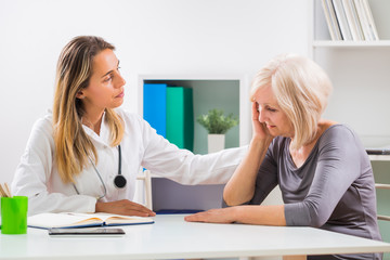 Female doctor consoling  her senior patient in office.