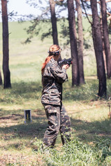 Girl in camouflage with a gun, plays laser tag in the forest. the player is aiming. Lasertag shooting game in open air. Military sport. Simulation of military operations