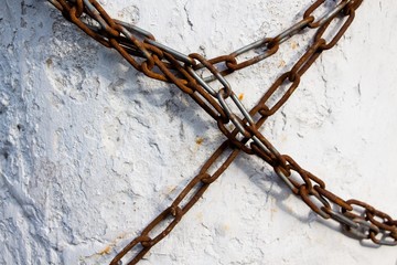 A long chain made of metal is covered with a little rust wrapped around the concrete wall and prohibits any movement. Indicates any prohibitions or dependencies.