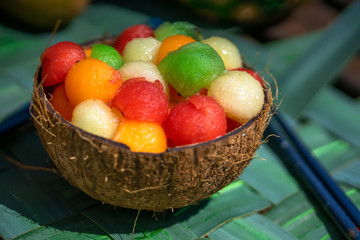 une coque de noix de coco remplie d'une salade de fruit avec des boules de différentes couleurs 