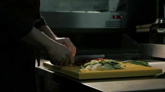 Close-up of chef hands cutting pepper for salad in restaurant kitchen