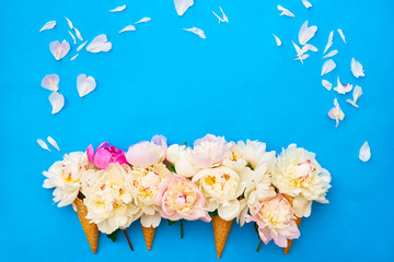 Waffle ice cream cones with white peony flowers on blue background. Summer concept. Copy space, top view