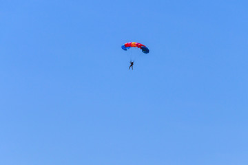 Parachutist descending with a parachute against blue sky