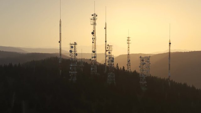 Antennas complex on a forested hill. Radio masts for telecommunication. Sunset.