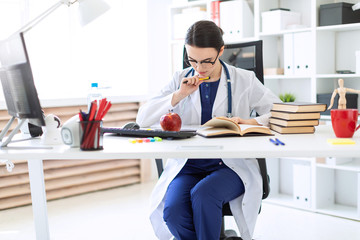 A beautiful young girl in a white robe sits at a computer desk, holds a pen and works with a notebook and documents.