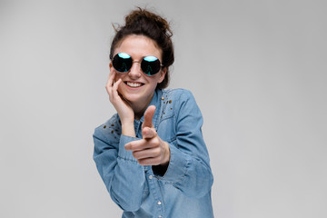 Young brunette girl in round glasses. Hairs are gathered in a bun. The girl points with her fingers.