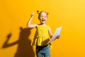 Girl with red hair on a yellow background. A beautiful girl is holding a pencil and a white sheet in her hands.