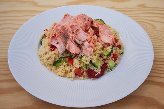 Detailed Picture of the fresh, tasty and healty couscous salad with poached salmon served on the simple white plate like light diner or lunch ideal for reduction diet.