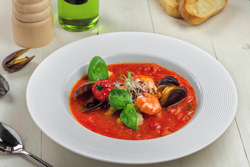 Excellent soup made of tomato and seafood on a rustic wooden table. Plate of healthy Italian meal.